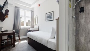 Ein Hotelzimmer mit Bett, Schreibtisch mit Stuhl, Fenster mit Vorhängen, einem gerahmten Bild an der Wand und einer Duschkabine.