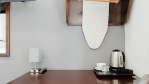 Ein Hotelzimmer mit einem Holztisch, einer Fernbedienung, einem weißen Bügelbrett, einem Wasserkocher und einer Tasse.