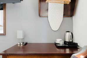 Ein Hotelzimmer mit einem Holztisch, einer Fernbedienung, einem weißen Bügelbrett, einem Wasserkocher und einer Tasse.