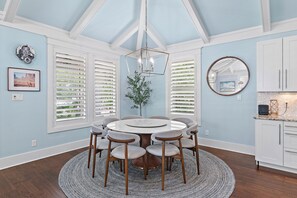 A dining room with a round table, six chairs, a chandelier, and a view through a window with shutters. - 🏡 Seagull’s Nest | Private Screened Pool | Quiet 30A Escape (Santa Rosa Beach)