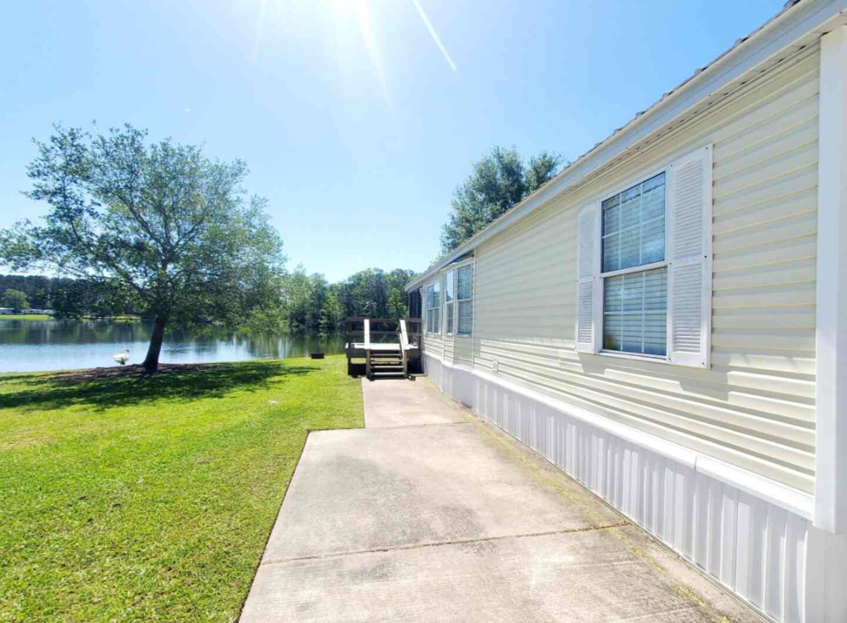 A mobile home with a concrete pathway leading to a dock by a lake.