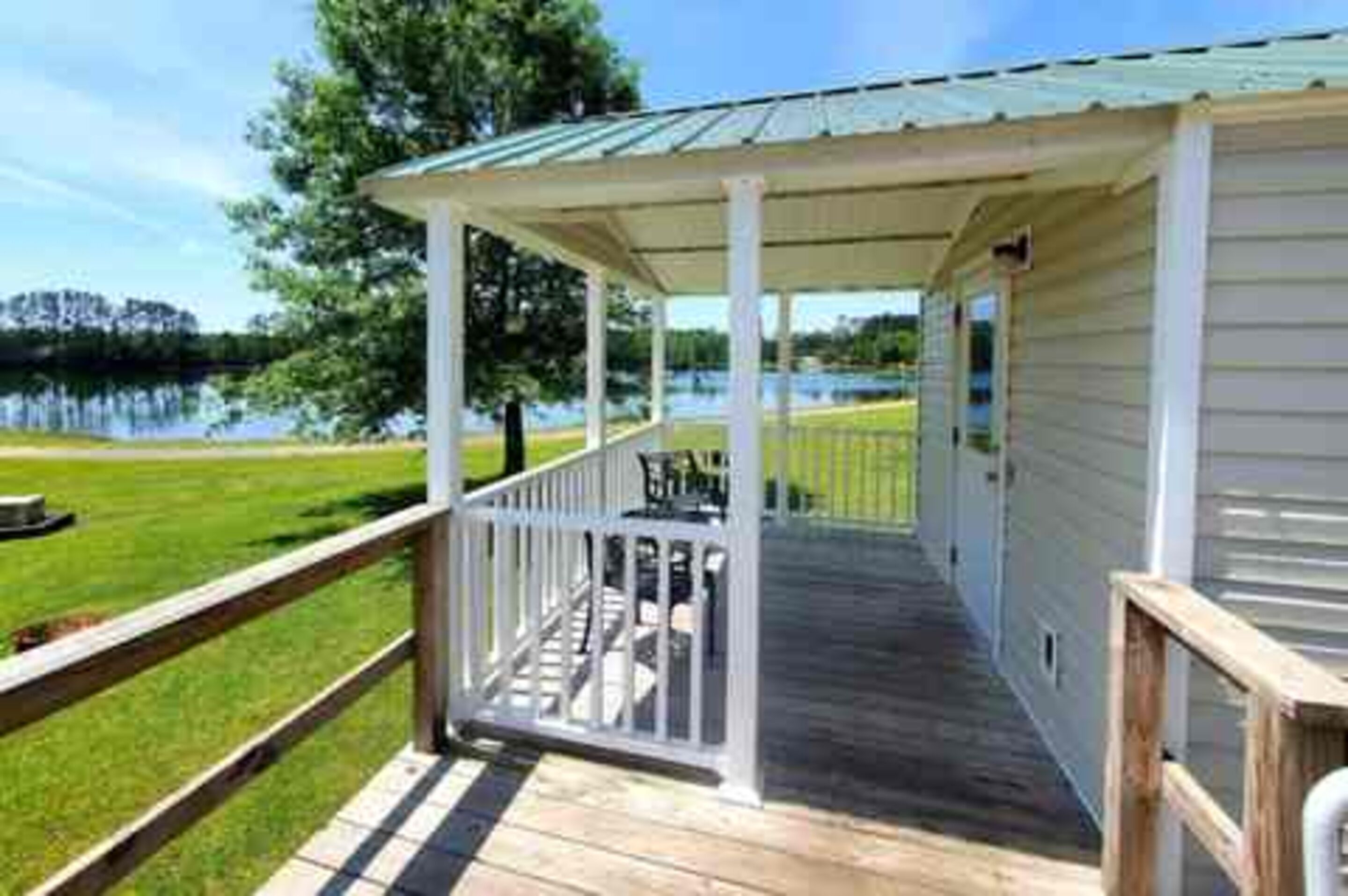 A covered deck with a railing, overlooking a body of water and a grassy area.