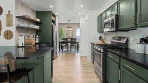 A modern kitchen with green cabinets, a central island, and a dining area with a table and chairs. - Mountain Views w/Hot Tub, 95” TV & Trail Access (Shenandoah Farms)