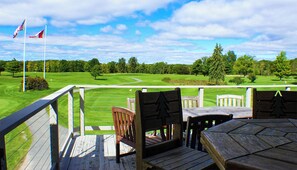 Eine Terrasse mit Holzbänken und einem Tisch mit Blick auf einen Golfplatz.