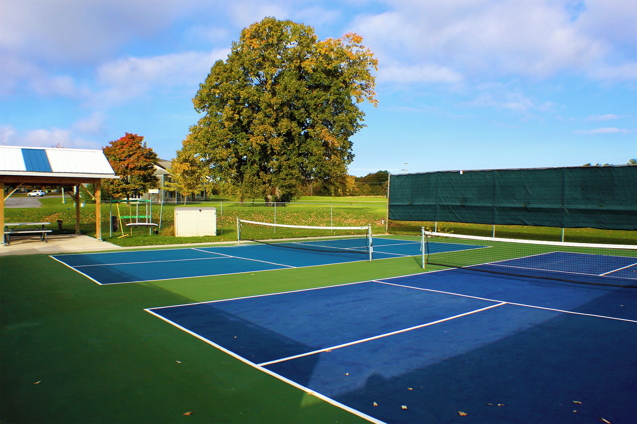 Una cancha de tenis con una red, un pabellón y un árbol grande.