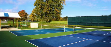 A tennis court with a net, a pavilion, and a large tree.