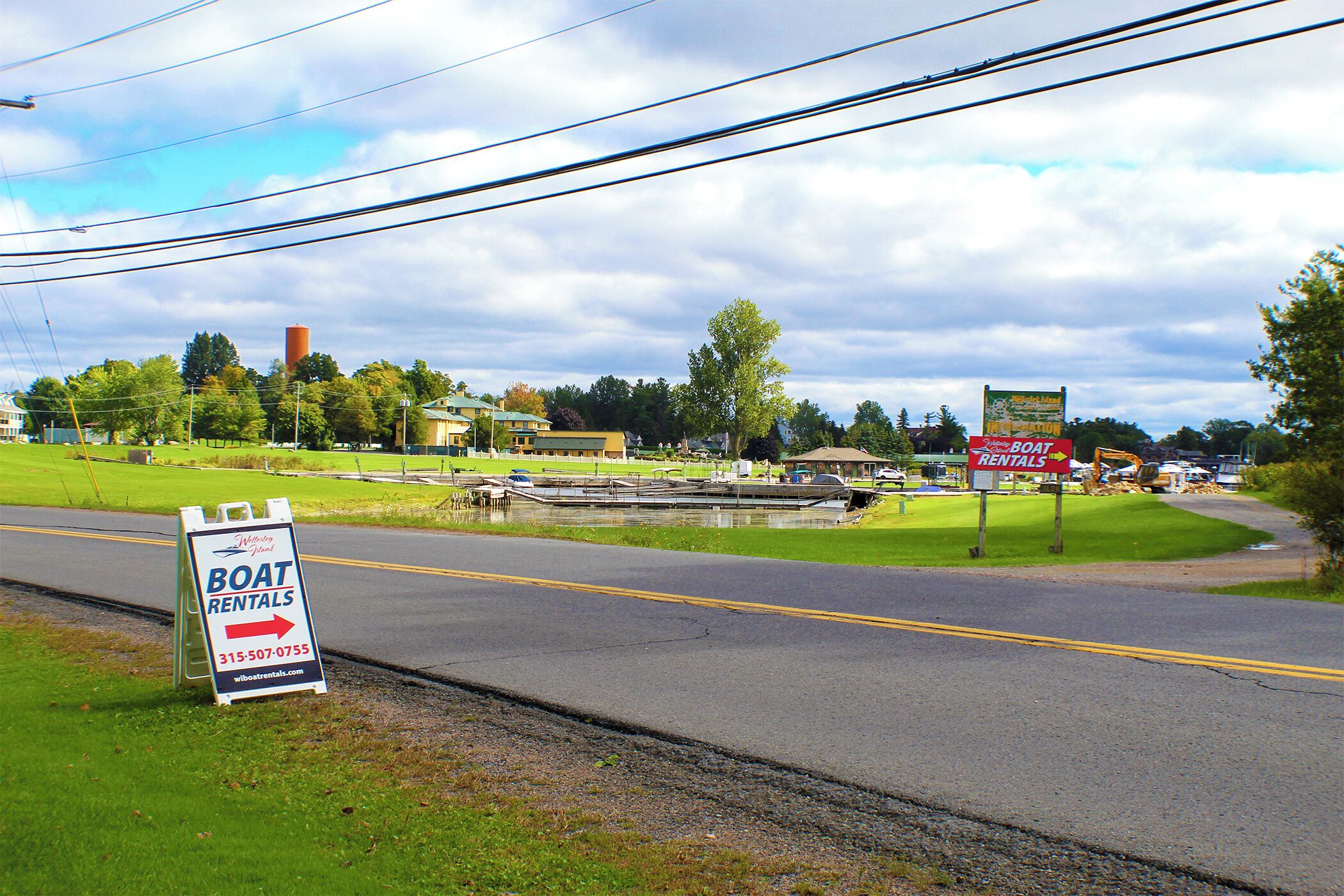 A road with a sign for boat rentals and a water body in the background.