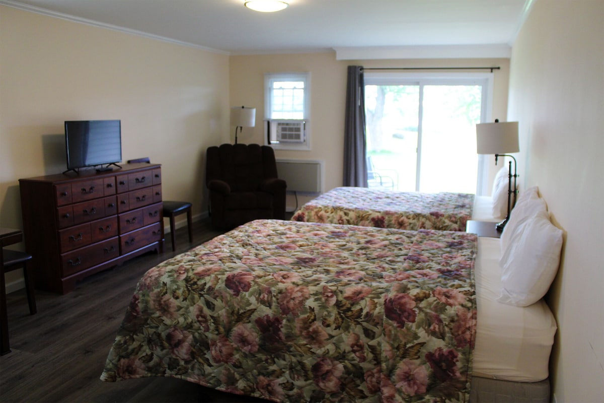 A hotel room with two beds, a dresser, a chair, a television, and a window with curtains.