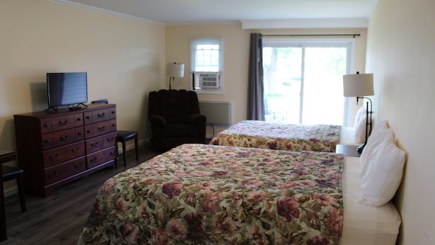 A hotel room with two beds, a dresser, a chair, a television, and a window with curtains. - Thousand Islands Country Club (Wellesley Island)