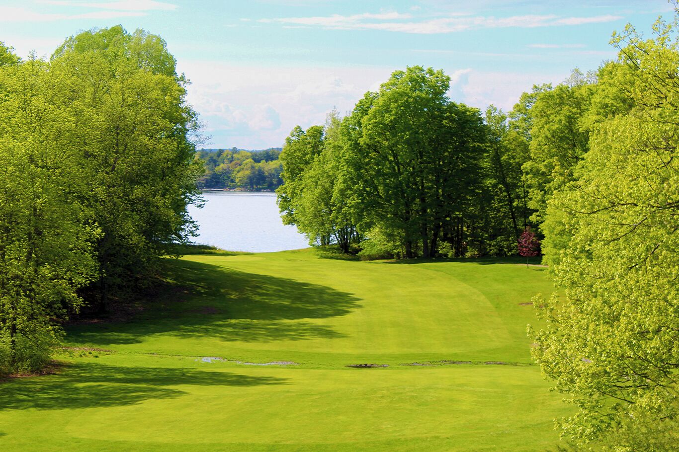 A golf course with a lake in the background, surrounded by trees.