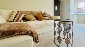 Een woonkamer met een bank, een glazen salontafel en een deur naar een buitenruimte.