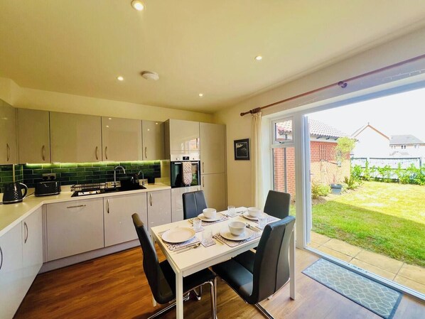 A modern kitchen with a dining area, featuring a large window, a dining table set for four, and a small outdoor garden visible through the window.