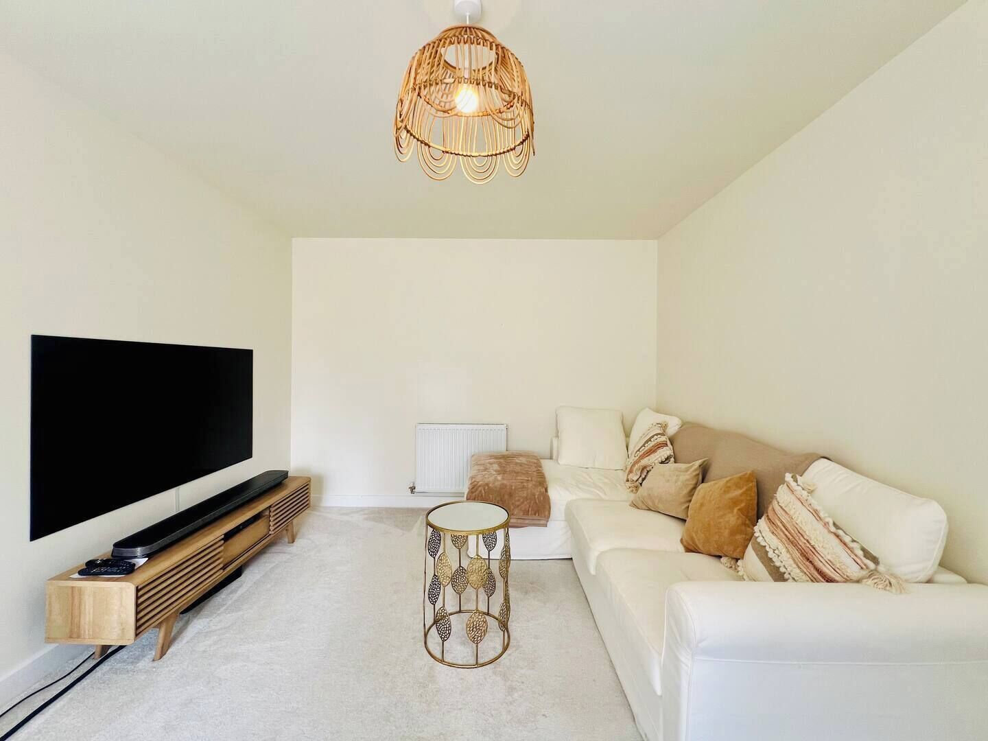 A modern living room with a flat-screen TV, a white sofa, a round coffee table, and a hanging light fixture.