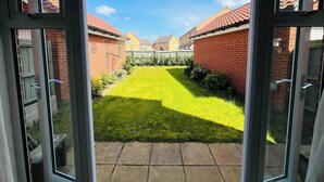 Uitzicht door een glazen deur op een achtertuin met gazon, bakstenen muren en een heldere lucht.