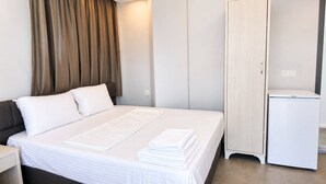 A hotel room with a bed, a wardrobe, a small white cabinet, and a curtain.