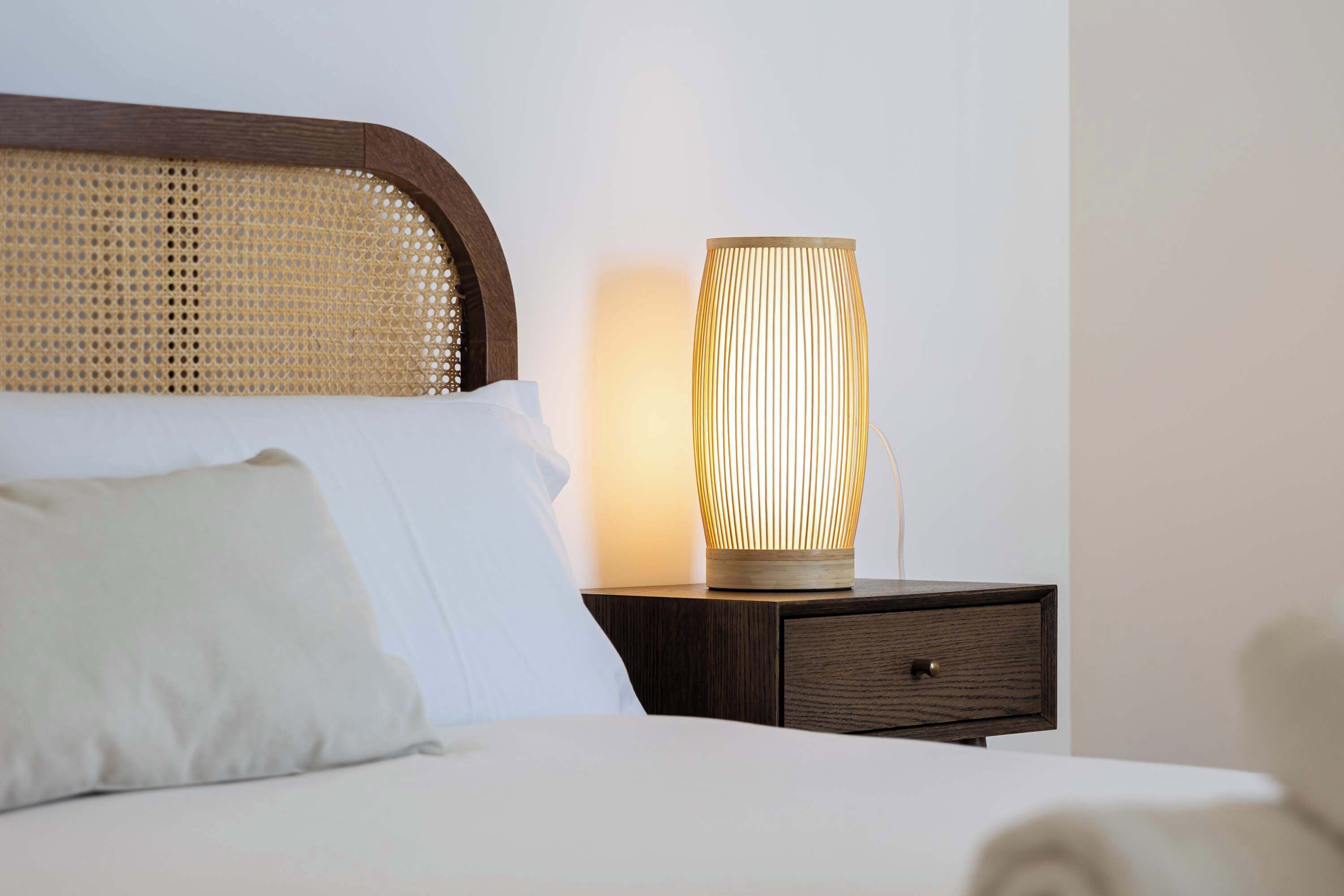 A bed with a headboard, a bedside lamp, a pillow, and a nightstand with a drawer.