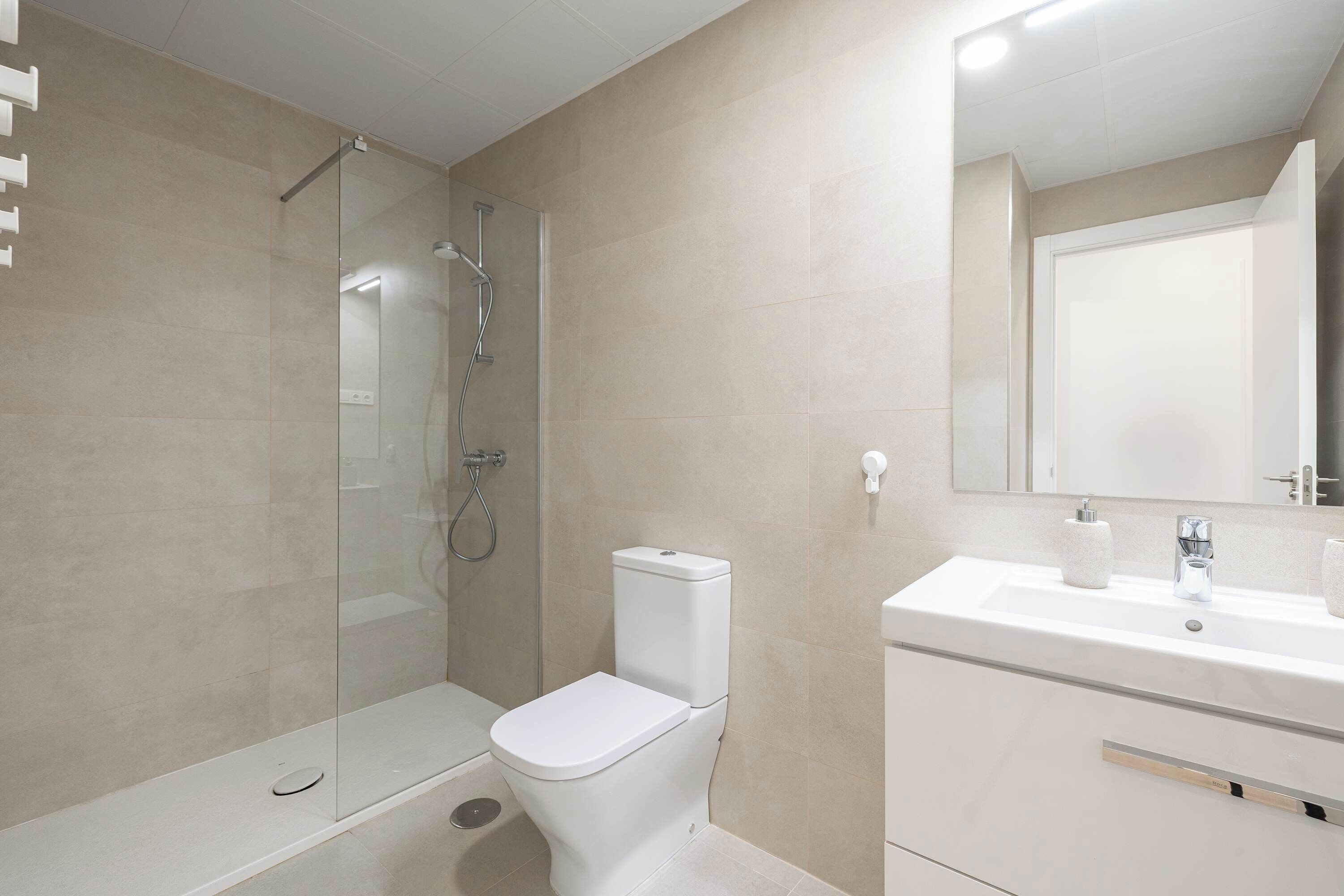 Une salle de bain moderne avec une douche à parois de verre, des toilettes blanches et un lavabo surmonté d’un miroir.