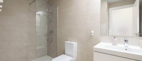 Une salle de bain moderne avec une douche à parois de verre, des toilettes blanches et un lavabo surmonté d’un miroir.