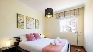 Un dormitorio con cama, mesitas de noche, una lámpara de pie y cuadros en la pared.