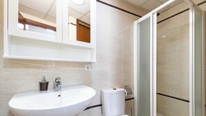 Un baño con lavamanos blanco, inodoro y cabina de ducha de vidrio.