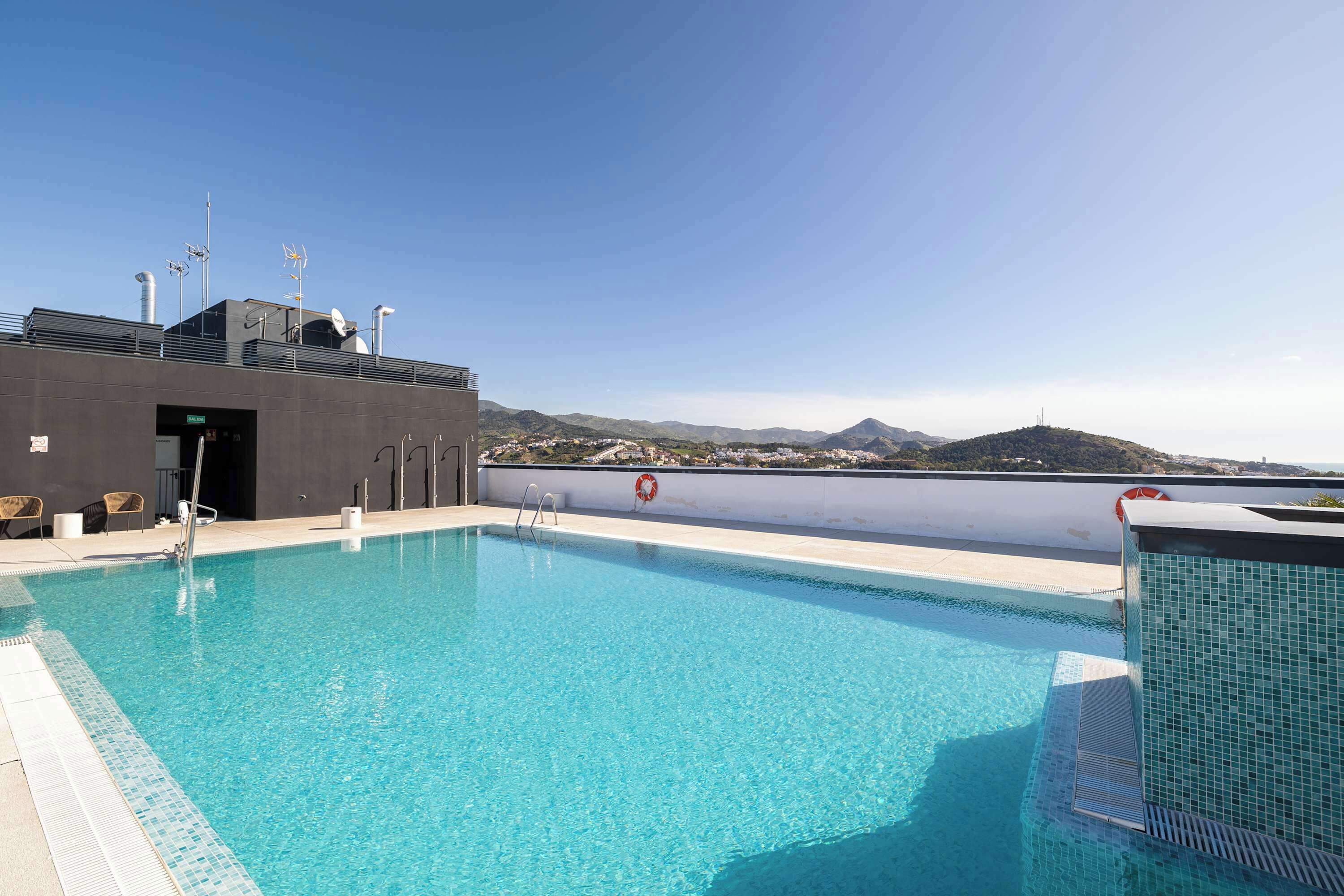 A rooftop swimming pool with a clear view of distant mountains, a lifebuoy, and a fire hose.