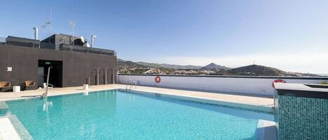 A rooftop swimming pool with a clear view of distant mountains, a lifebuoy, and a fire hose.