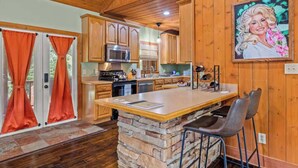 A kitchen with wooden cabinets, a central island, and a stone accent wall. - 2 Cabins in One- Mtn Views - Hot Tub - Fenced Yard (Pigeon Forge)