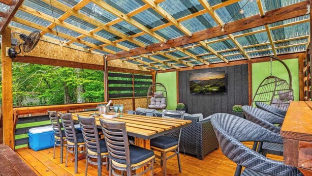 Un espace extérieur abrité, aménagé pour les repas, avec une table en bois, des chaises et une chaise suspendue en forme de balançoire.
