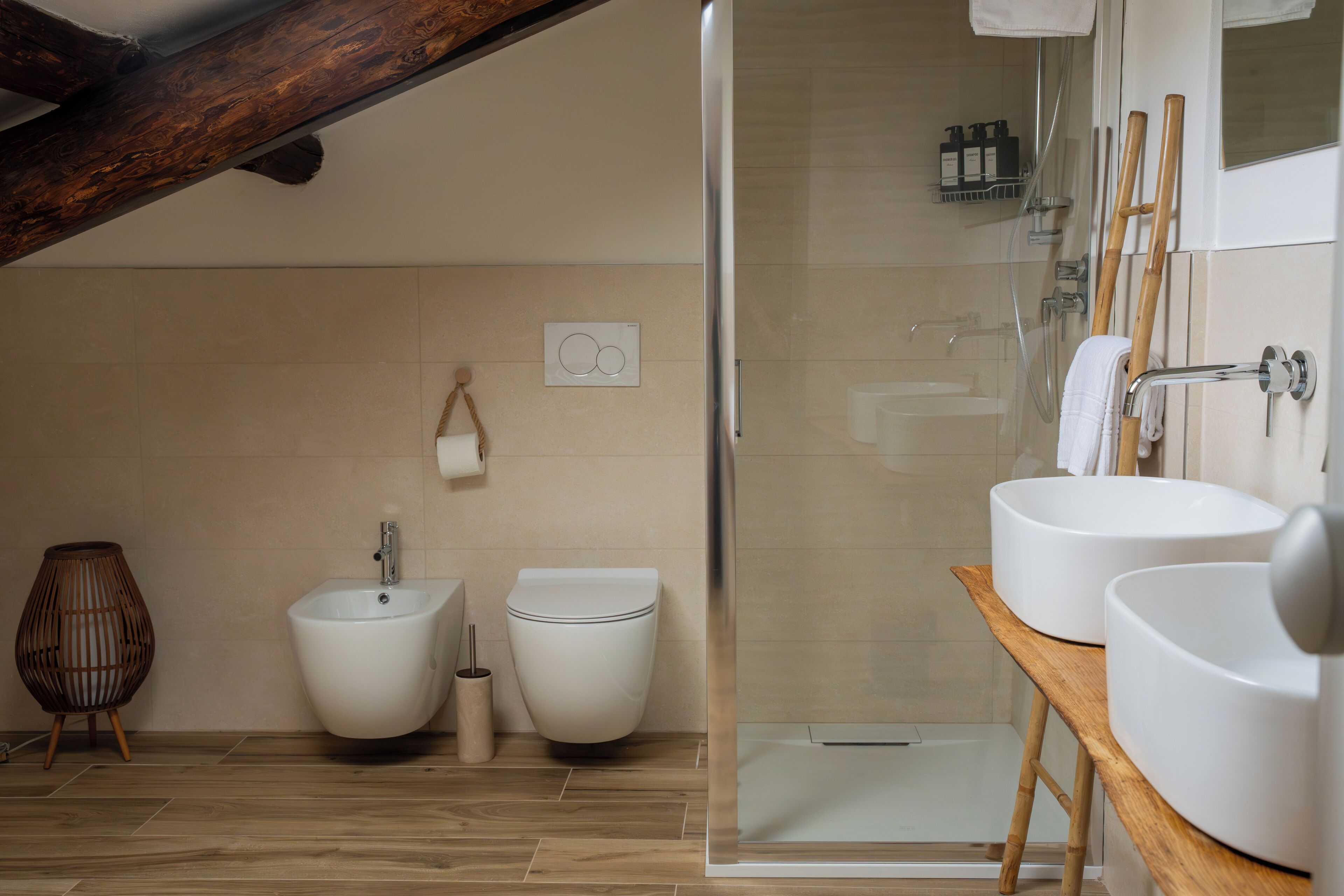 Une salle de bain moderne équipée d’une douche, de deux toilettes, d’un bidet et d’un meuble-lavabo en bois avec deux vasques.