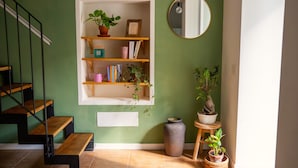A staircase with wooden steps and metal railings, a wall-mounted shelf with books and plants, a round mirror, and a potted plant on a small table.