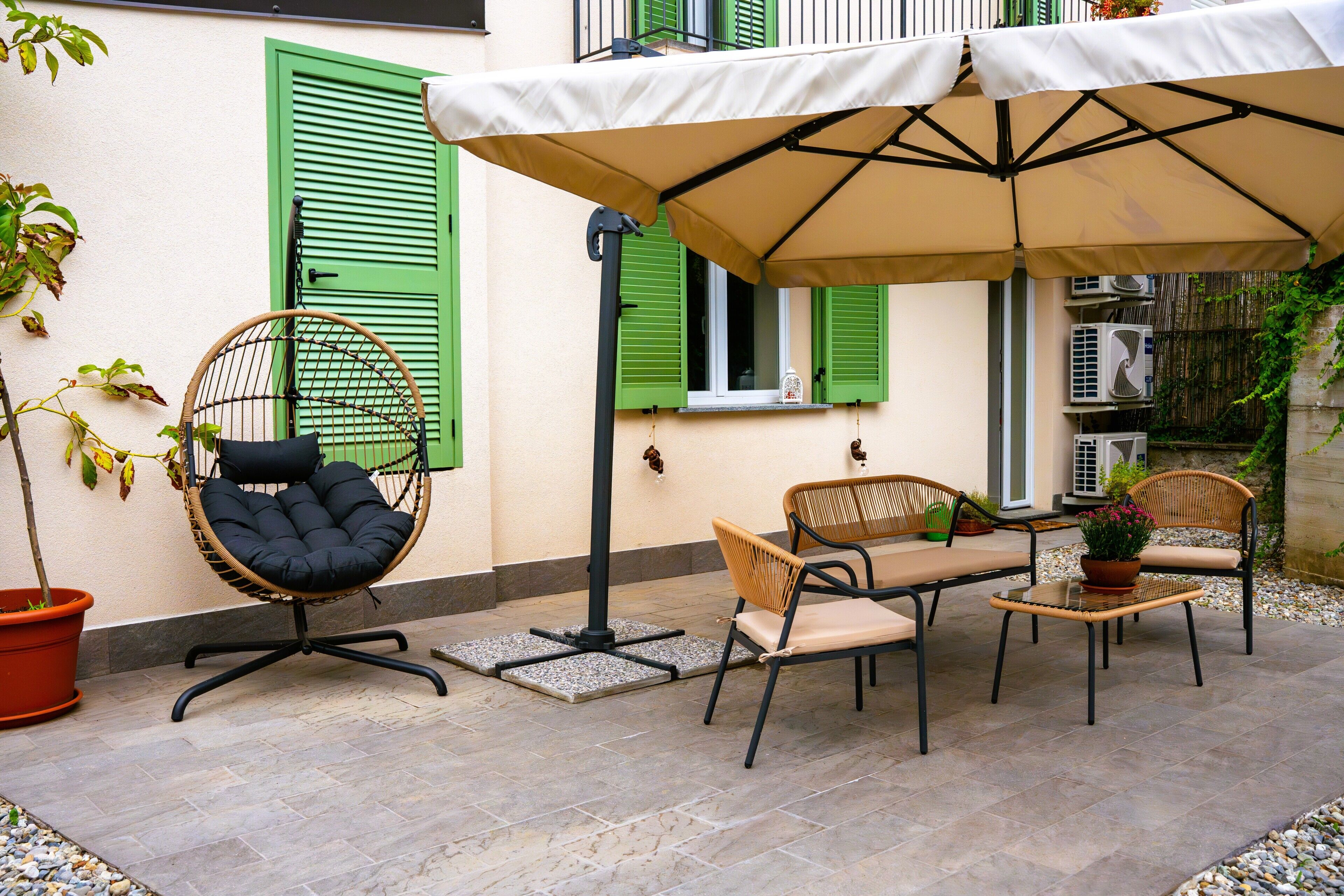 An outdoor patio with a table and chairs, a hanging chair, and a large umbrella providing shade.