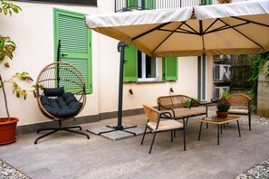Un patio exterior con mesa y sillas, una silla colgante y un gran paraguas que da sombra.
