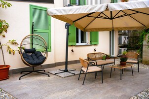 Un patio exterior con mesa y sillas, una silla colgante y un gran paraguas que da sombra.