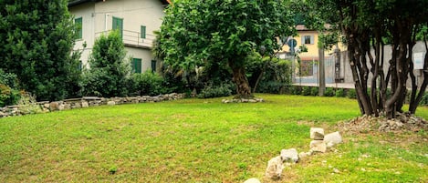 A grassy area with a stone wall, trees, and a building with a red roof.