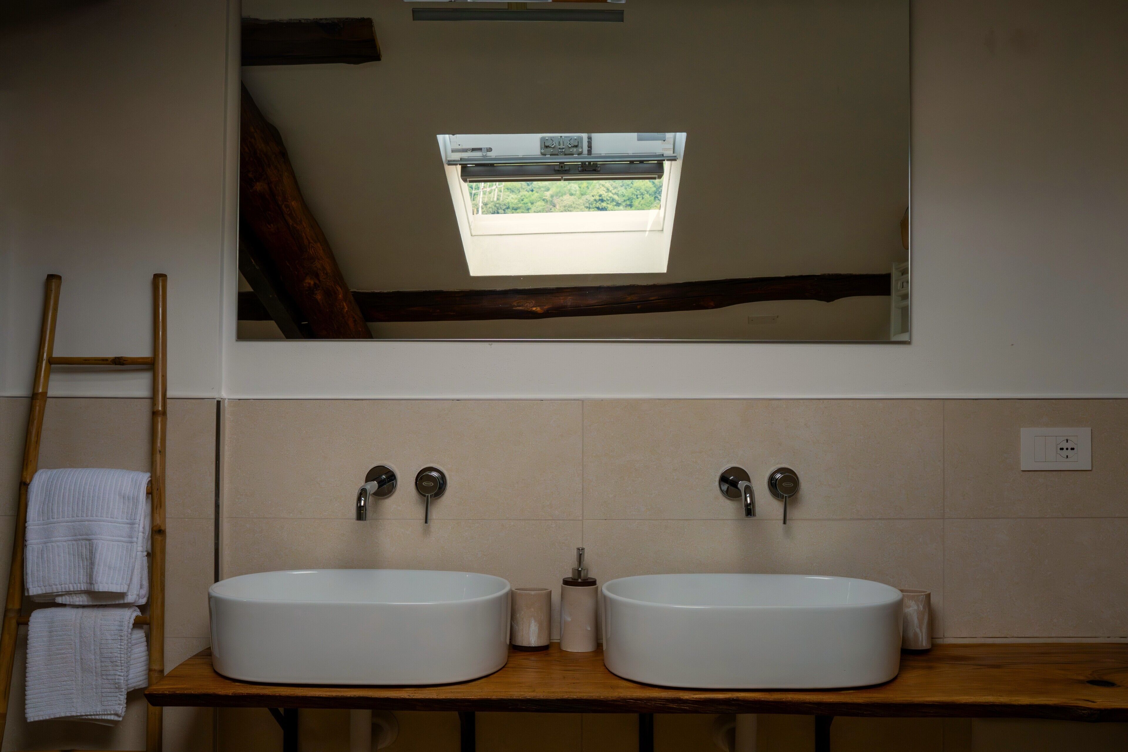 Un baño con dos lavamanos redondos, una escalera de madera y un espejo que refleja una ventana con vistas a la vegetación.