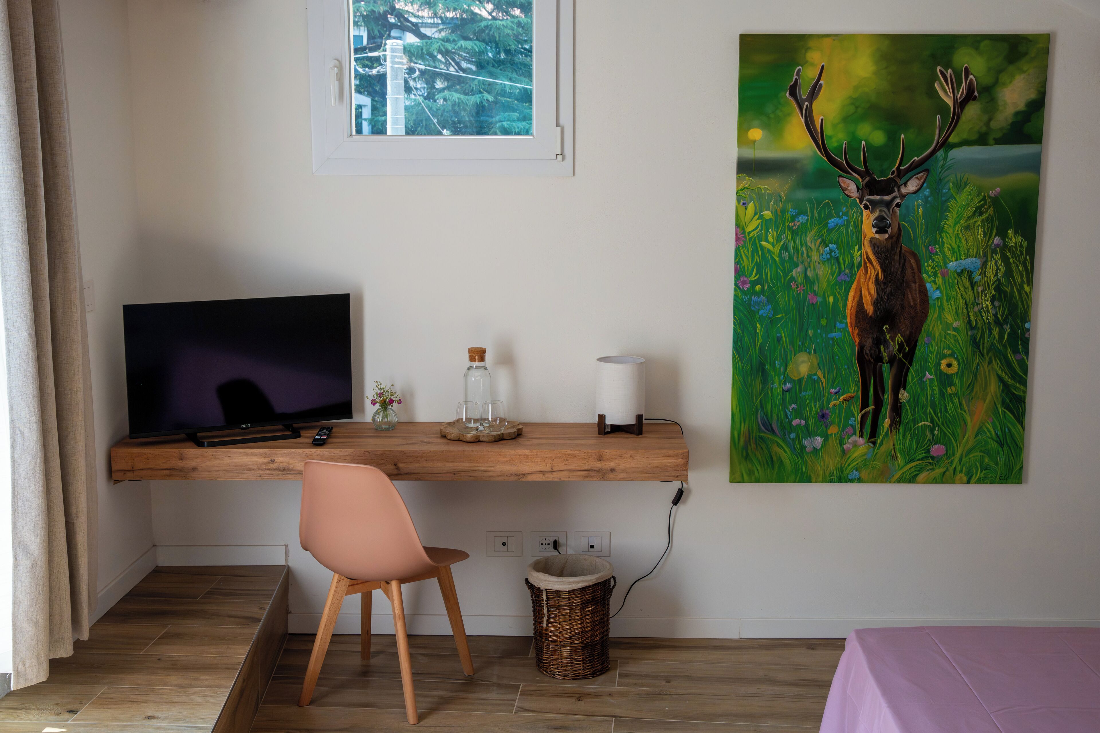 Una stanza con una scrivania in legno, una televisione, una sedia, un quadro raffigurante un cervo e una finestra.