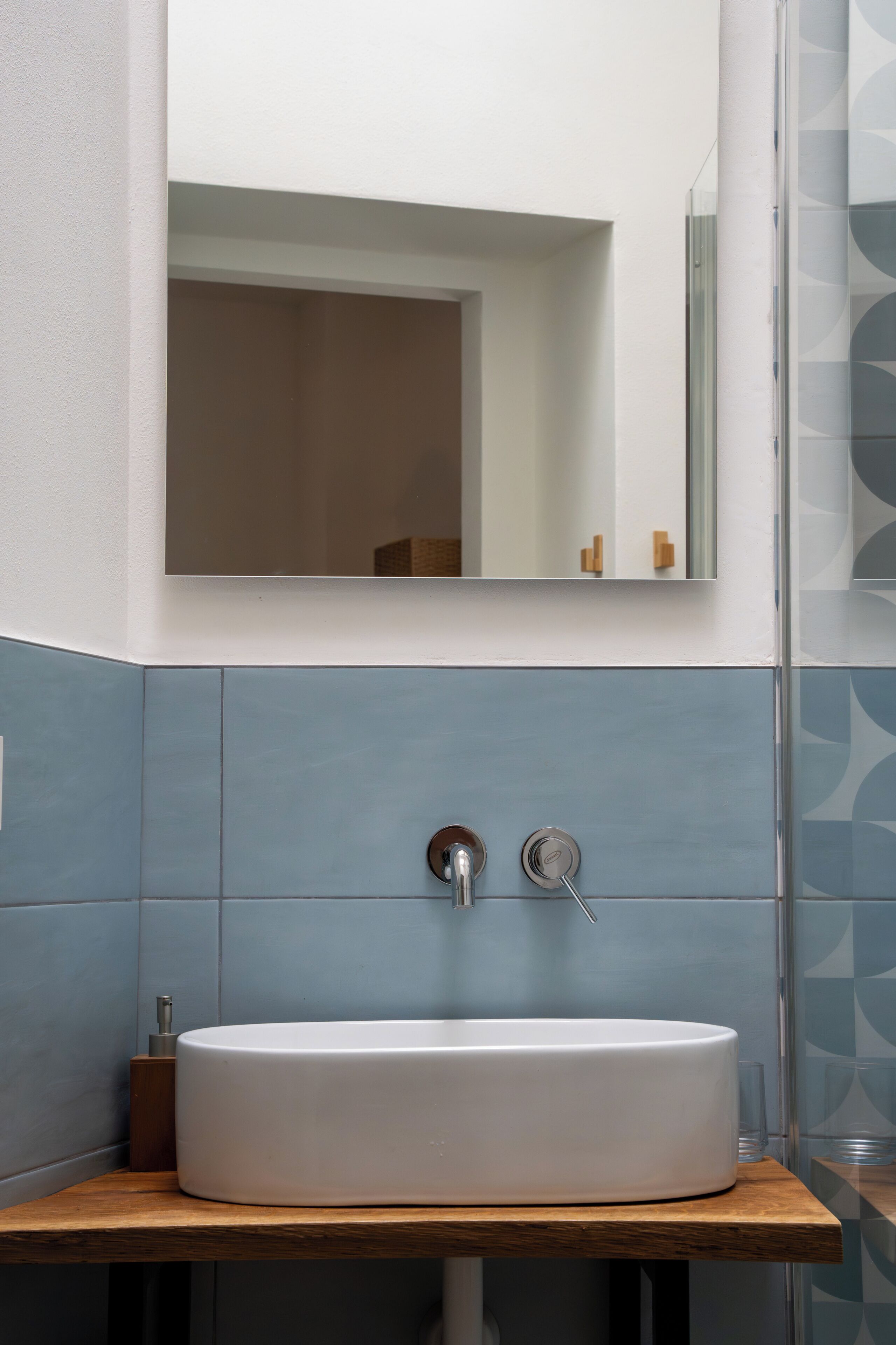 A bathroom with a white sink, a mirror above it, and blue tiled walls.
