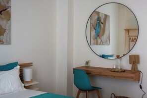 Un dormitorio con cama, escritorio, silla, espejo redondo y un cuadro en la pared.