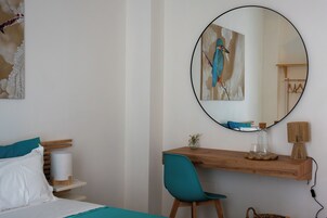 Un dormitorio con cama, escritorio, silla, espejo redondo y un cuadro en la pared.