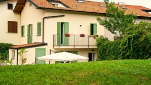 A two-story building with a balcony, a small garden area with a white umbrella, and a green hedge. - Barzy Urban Country House (Como)