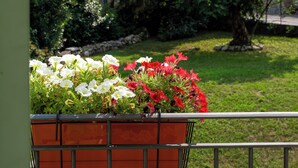 A balcony with a flower planter, a house in the background, and a grassy area with trees. - Barzy Urban Country House (Como)
