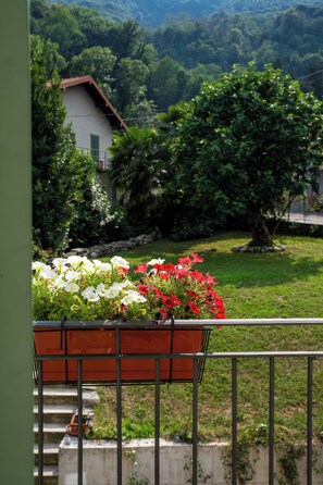 A balcony with a flower planter, a house in the background, and a grassy area with trees.