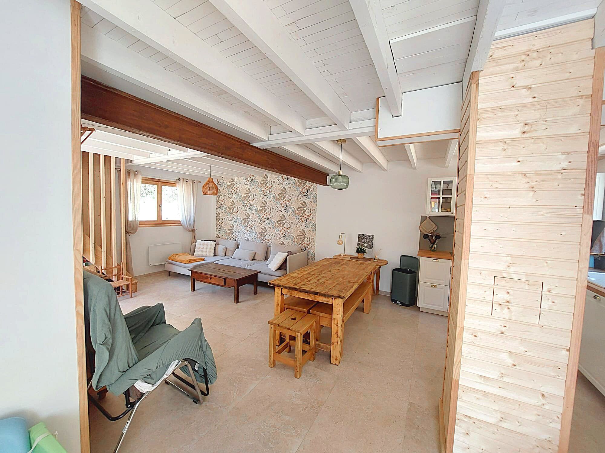 A room with a wooden dining table, a sofa, and a kitchen area with wooden cabinets.
