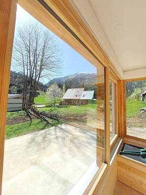 Une pièce dotée de grandes fenêtres, d’un sol en béton et offrant une vue sur un paysage rural avec des arbres et un bâtiment.