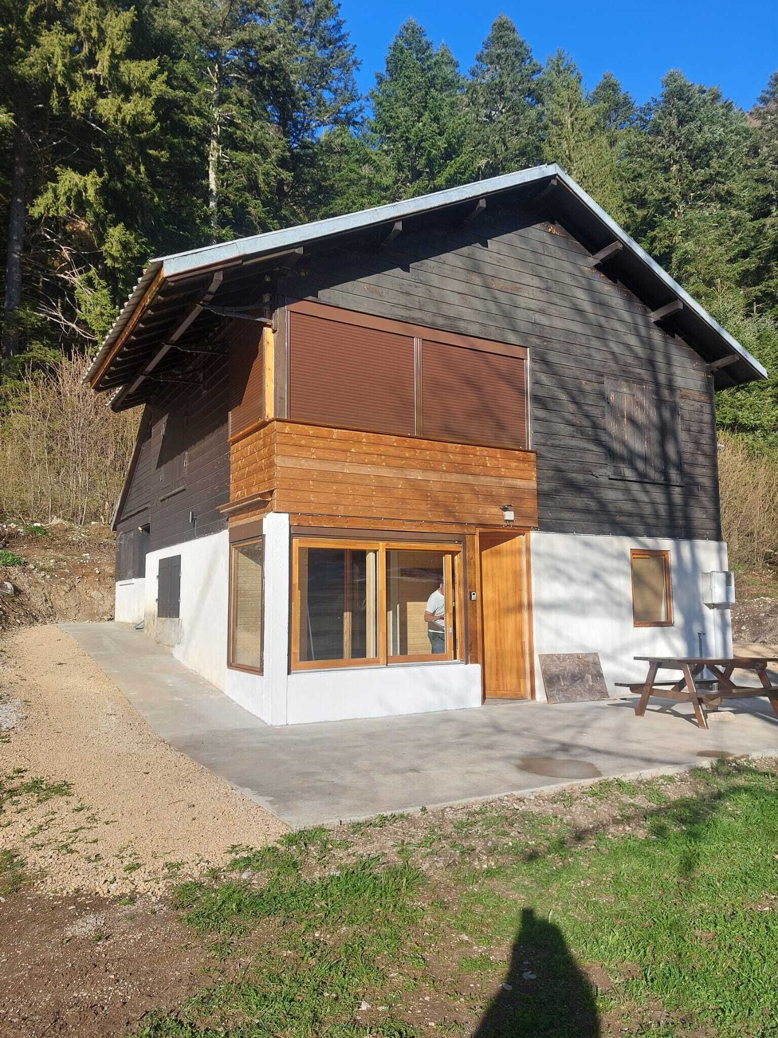 A two-story cabin with a balcony, large windows, and a picnic table.