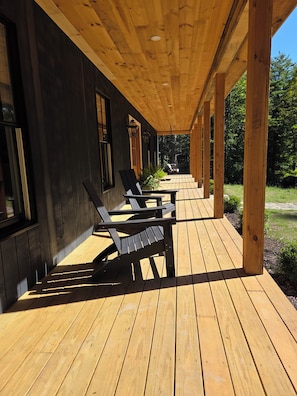 Eine überdachte Holzterrasse mit Sitzgelegenheiten und Blick auf ein bewaldetes Gebiet.