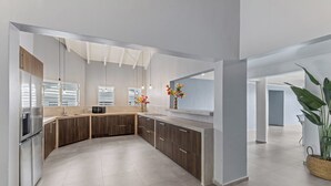Une cuisine moderne dotée d’un îlot central aux lignes courbes, d’appareils électroménagers en acier inoxydable et d’une grande fenêtre avec des stores.