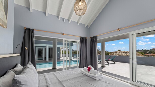 Une chambre dotée d’un grand lit, offrant une vue sur une piscine et comprenant un balcon avec des chaises longues.