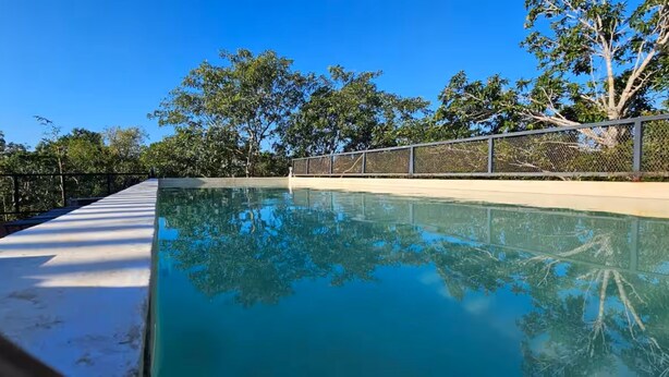 Una piscina con agua cristalina azul, rodeada por una valla y árboles.