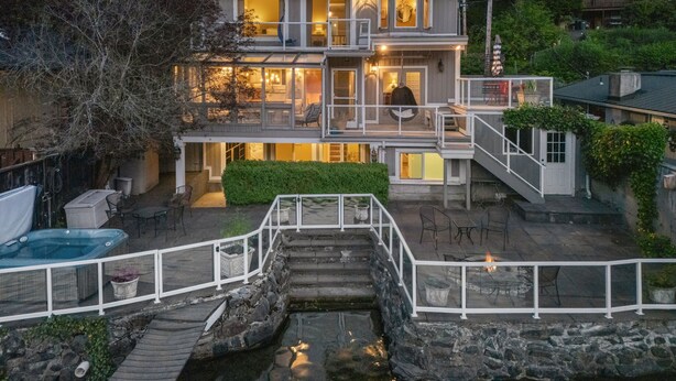 Een huis met twee verdiepingen, met een stenen trap die leidt naar een terras, omringd door groen.